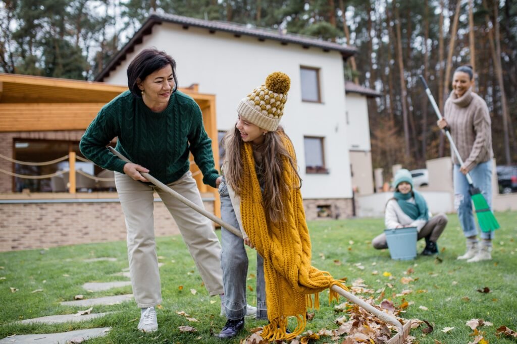 Happy little girls with grandmother and mother cleaning up garden from leaves in autumn